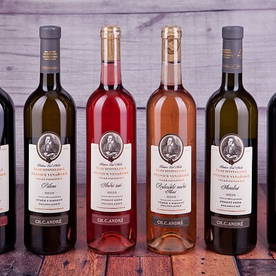 Detailní záběr na různé odrůdy vín ve skleněných lahvích s etiketami, umístěné na dřevěném podkladu, vhodné pro víno, degustace a vinařství.