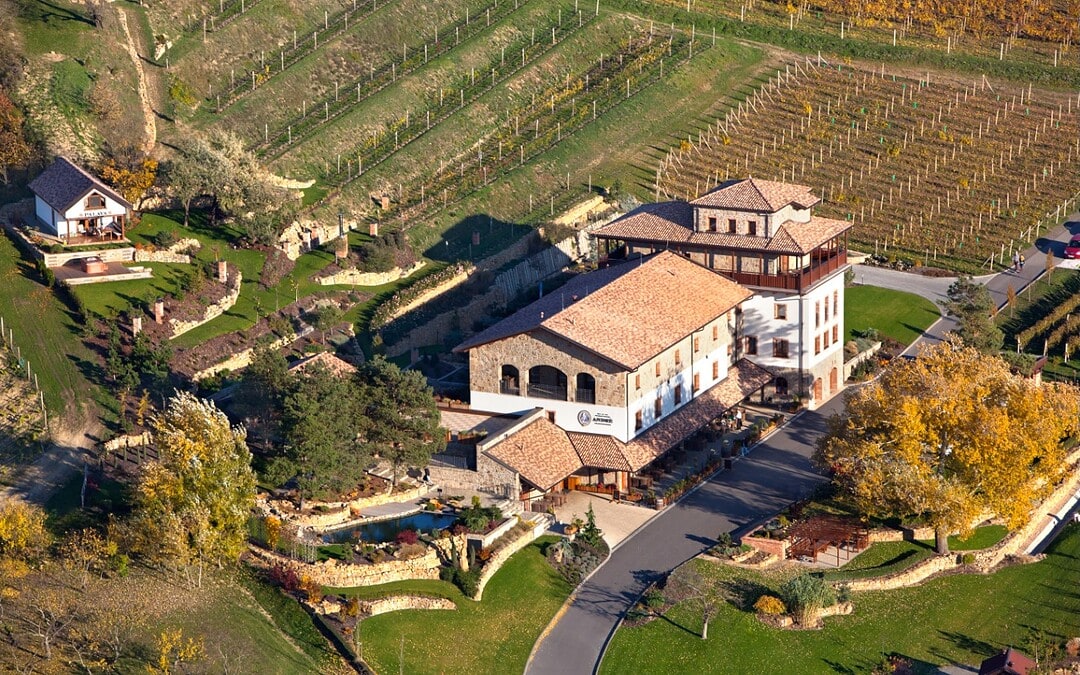 Bird's-eye view of BrnoOpen wine estate with vineyards, lush gardens, and modern wine tasting facility in a scenic rural setting.