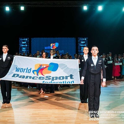 Skupina mladých tanečníků na taneční soutěži Brno Open 2020 drží vlajku World DanceSport federace na tanečním parketu.