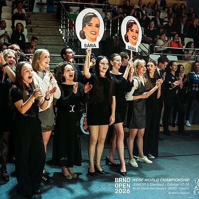 Skupina nadšených diváků a soutěžících na BrnoOpen 2026, sportovní akce s fanoušky a soutěžícími držícími portréty a plakáty, v sportovním prostředí.