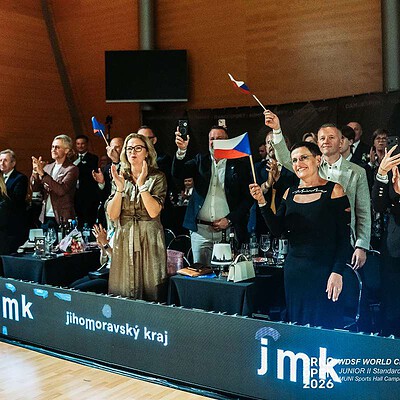 Skupina lidí na sportovní akci v Brně, někteří mávají vlajkami a sledují zápas nebo ceremoniál, s logem Jihomoravského kraje a sportovními značkami.