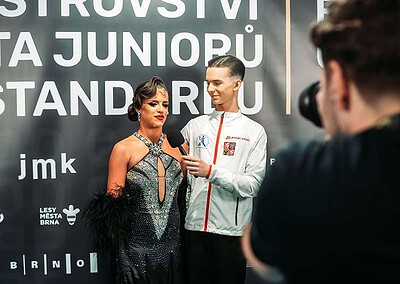 Dva tanečníci na soutěži BrnoOpen 2023, rozhovor s moderátorem, pozadí s nápisem a logy sponzorů, sportovní akce v Brně.
