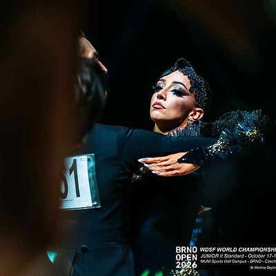 Dívka v černém tanečním kostýmu na soutěži BrnoOpen 2026, elegantní a soustředěná, s dramatickým make-upem a účesem, v tanečním prostředí s tmavým pozadím.