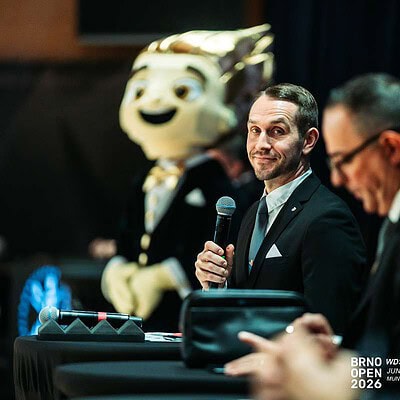 Muž s mikrofonem na konferenci BrnoOpen 2026, v pozadí maskot a další řečníci, profesionální atmosféra sportovní události.