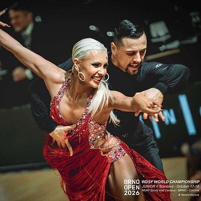 Duo tanečníků v elegantním vystoupení na Brno Open 2026, s výraznými pohyby a výrazem radosti, v tanečním prostředí s diváky a soutěžní scénou v pozadí.