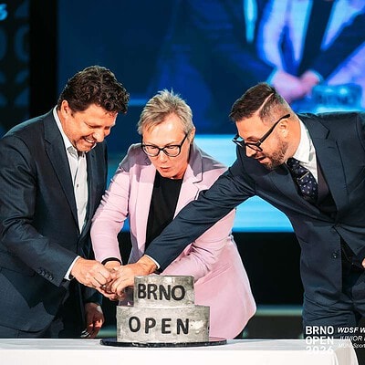 Tři šachisté slavnostně lámou dort s nápisem Brno Open na mezinárodním šachovém turnaji v Brně, Česká republika.