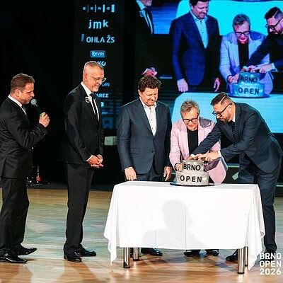 Skupina mužů na pódiu při oficiálním zahájení BrnoOpen 2026, podepisující dokumenty, s velkým displejem v pozadí.
