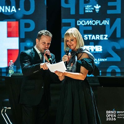 Dva moderátoři na pódiu s mikrofony během BrnoOpen 2026, v pozadí logo srdce a texty o sportovním turnaji.