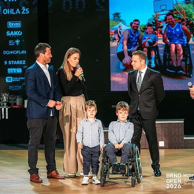Skupina lidí na pódiu během události BrnoOpen 2026, včetně osob s postižením, s velkým displejem v pozadí zobrazujícím týmové fotografie.